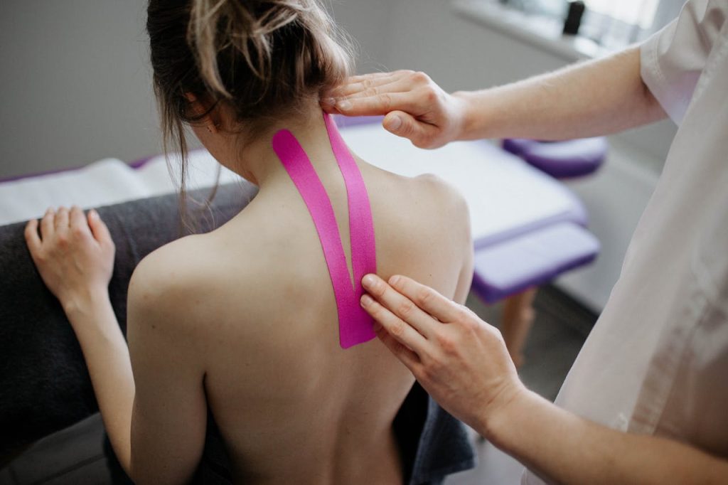 A healthcare professional applies kinesiology tape on a womans neck for therapeutic treatment.